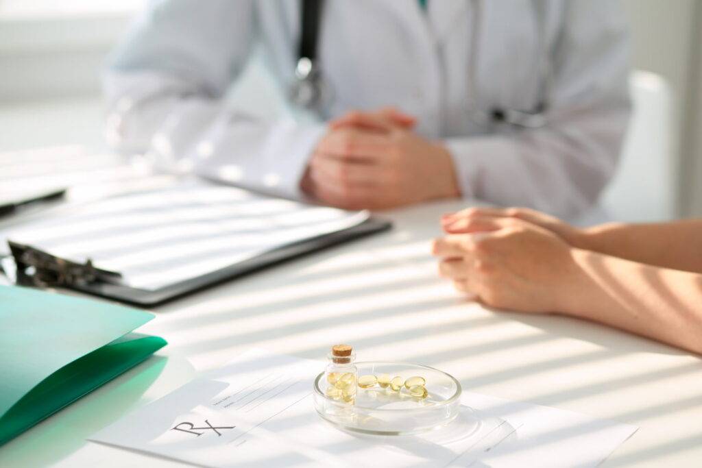 Paciente e médico conversando em uma mesa com papéis e medicamentos importados.