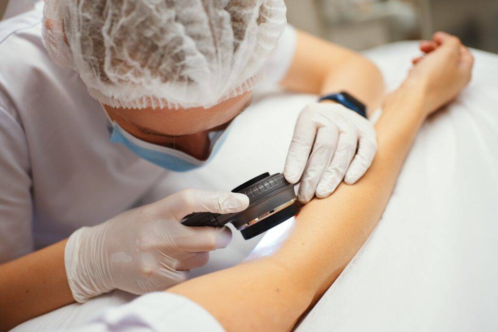 Dermatologista examinando a pele do braço de paciente, representando início do tratamento câncer de pele.