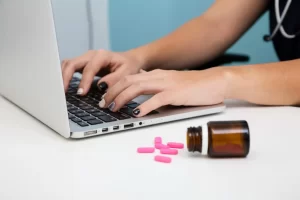 mãos brancas femininas de unhas pintadas digitando em um notebook pesquisando onde comprar medicamentos importados no Brasil.