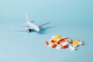 Imagem de um avião e diversas pílulas de remédio, simbolizando a importação de medicamentos por pessoa física.