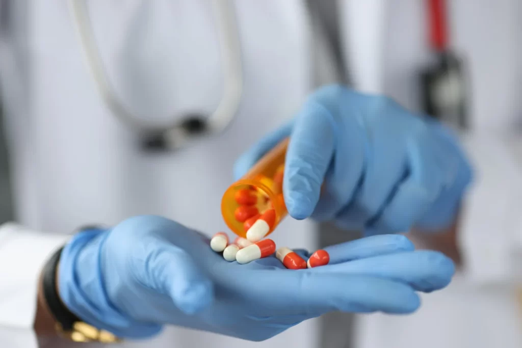 Médico com luvas azuis segura pílulas, ilustrando a diferença entre medicamento manipulado e industrializado