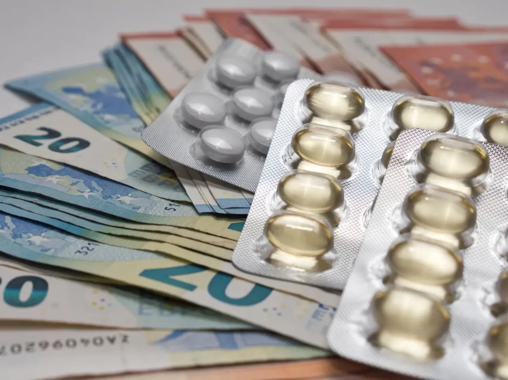 Imagem de comprimidos em torno de cédulas de dinheiro, simbolizando o reembolso de medicamentos importados.