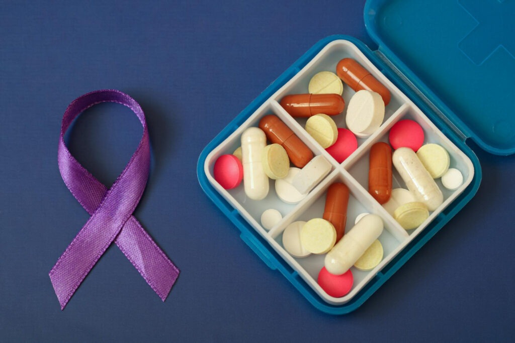 medicamentos oncológicos de alto custo ao lado um laço roxo representando tratamento de câncer