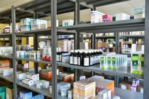 Prateleiras metálicas organizadas com diversos medicamentos e produtos farmacêuticos em estoque de farmácia.