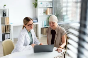 Médico em consulta com paciente revisa opções de tratamento oncológico em laptop em ambiente clínico.