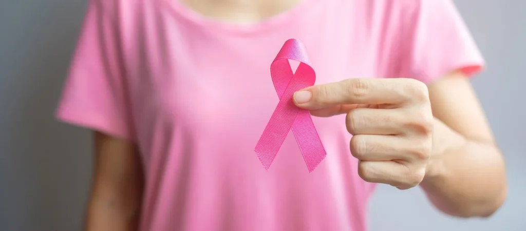 Médica segura laço rosa ao lado de comprimidos, representando medicamentos importados para câncer de mama.