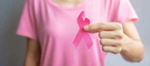 Médica segura laço rosa ao lado de comprimidos, representando medicamentos importados para câncer de mama.